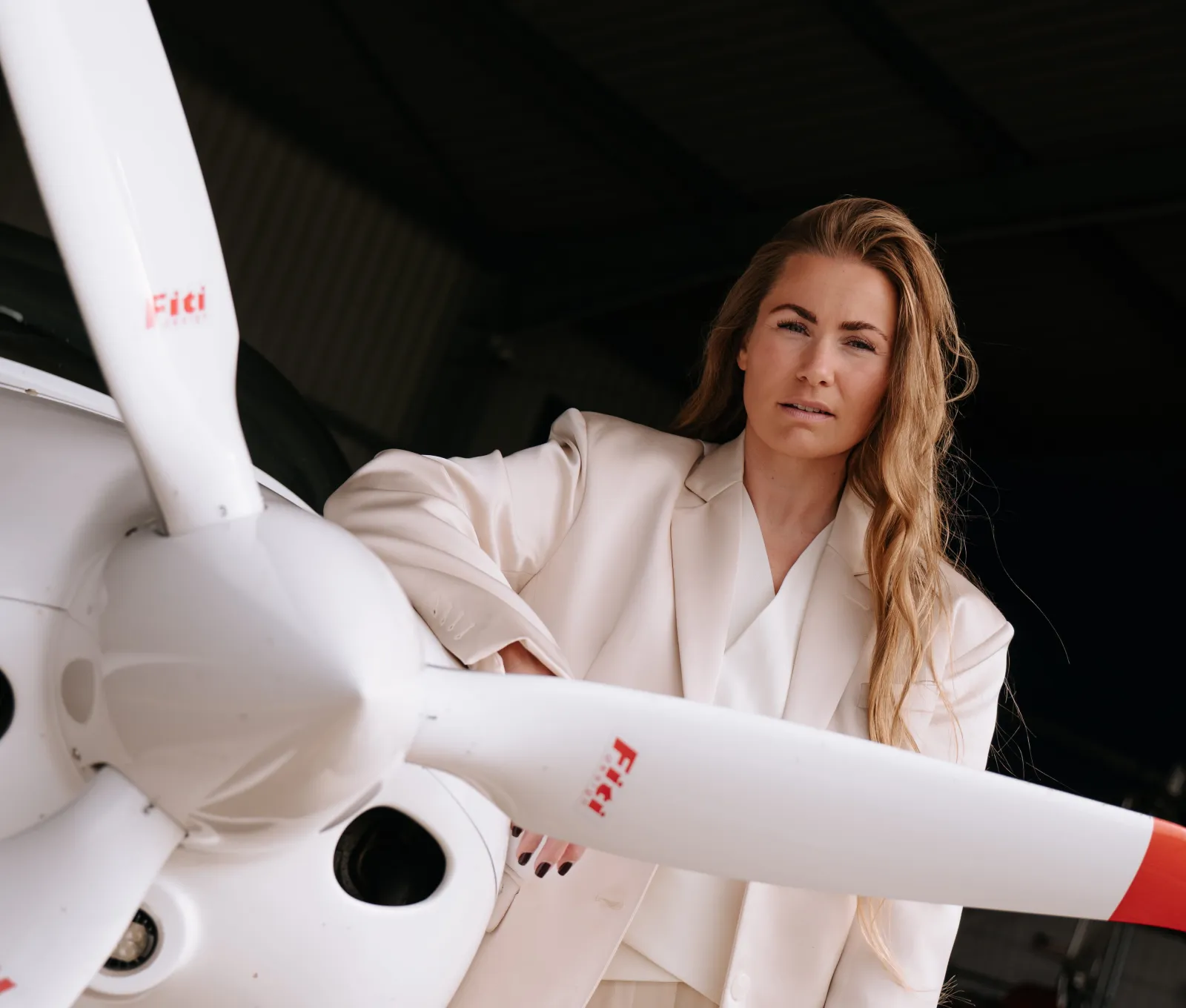 Clenda Moen in een wit pak naast de propeller van een klein vliegtuig