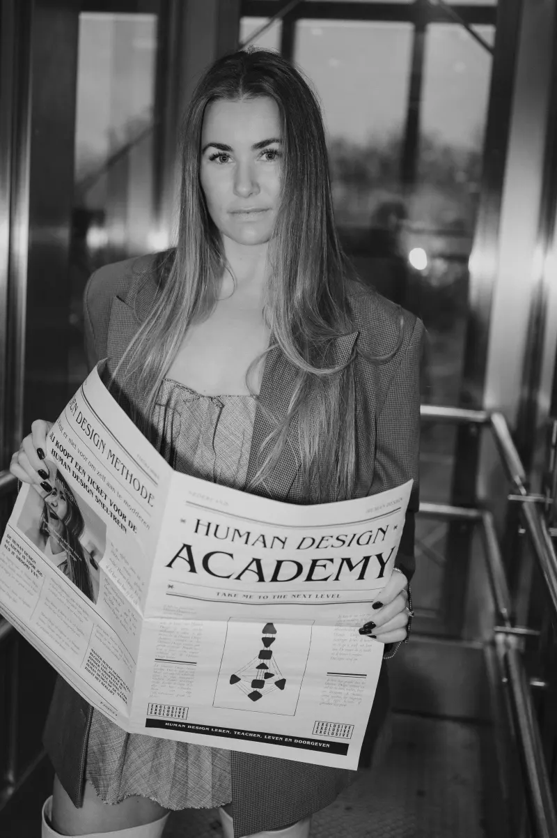 Zwart-witfoto van Clenda Moen met de Human Design Academy-krant in een lift