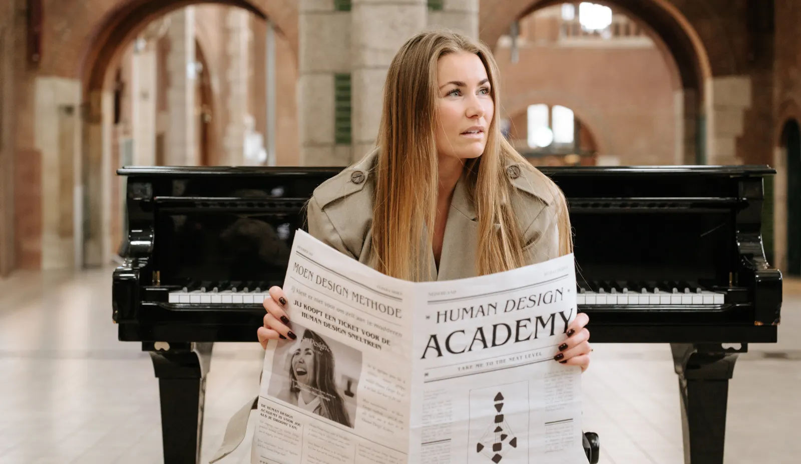 Clenda Moen zit met de Human Design Academy-krant voor een vleugel in een stationshal